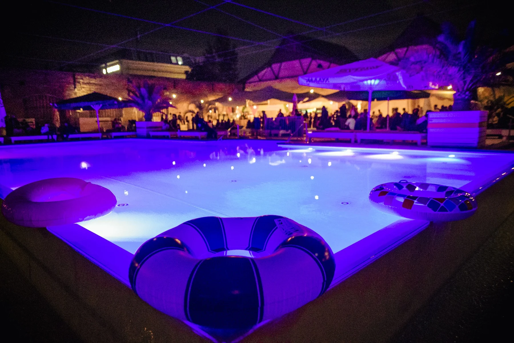 Beleuchteter Pool mit Schwimmringen und Gästen am Abend